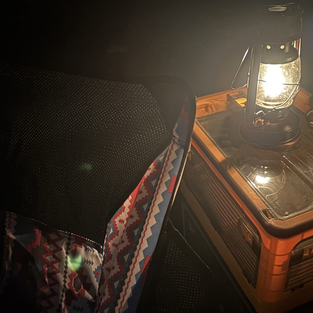 暗い中で灯るランタンとキャンプ用チェアのある空間