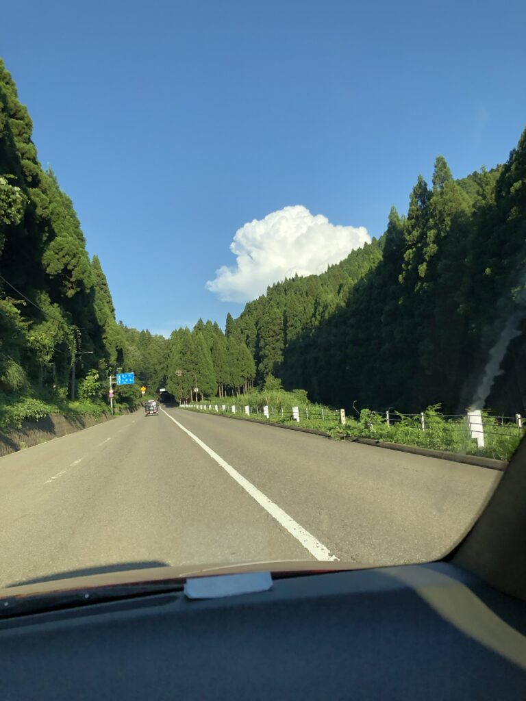 青空の下、山に囲まれた道を車で走る風景