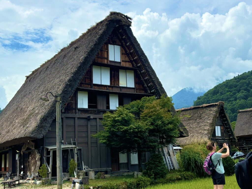 白川郷の大きな合掌造りの建物と夏の空、立ち止まって景色を見る人