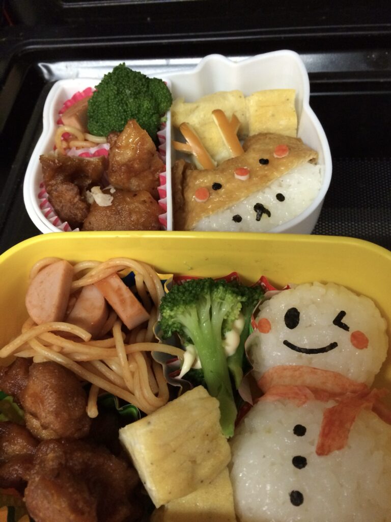 雪だるまの顔をつけたごはんとおかずを詰めた子どもの手作り弁当